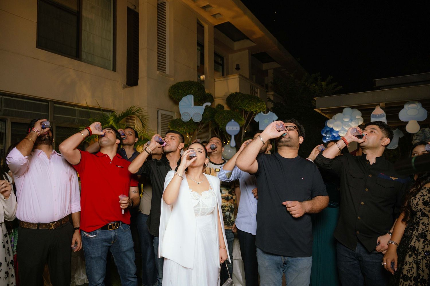 Group of people raising drinks and looking up at the sky during an outdoor evening celebration or party.