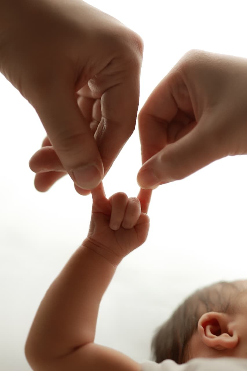 Two adult hands gently holding a newborn baby's tiny hand, symbolizing love and parental bond.