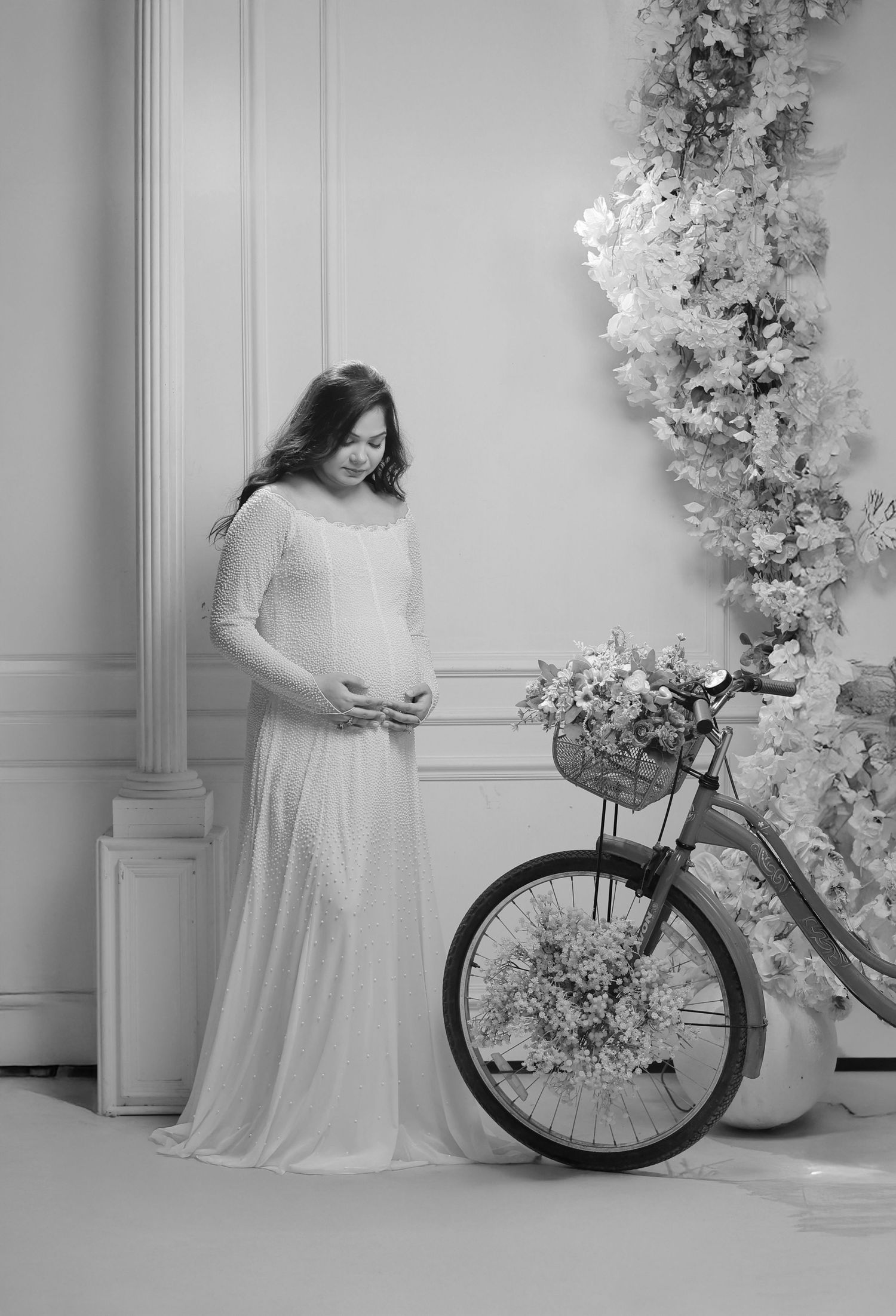 A romantic maternity photo series in black and white featuring a floral backdrop and vintage bicycle.