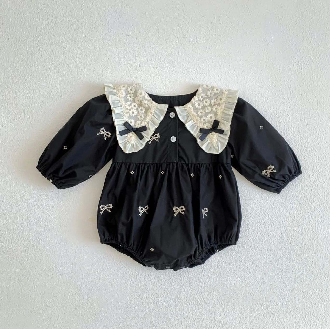 Black silk dress with white lace peter pan collar and small embroidered bow details arranged in a row.