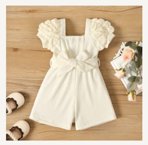 White ribbed cotton baby romper with ruffled collar displayed on wooden background.