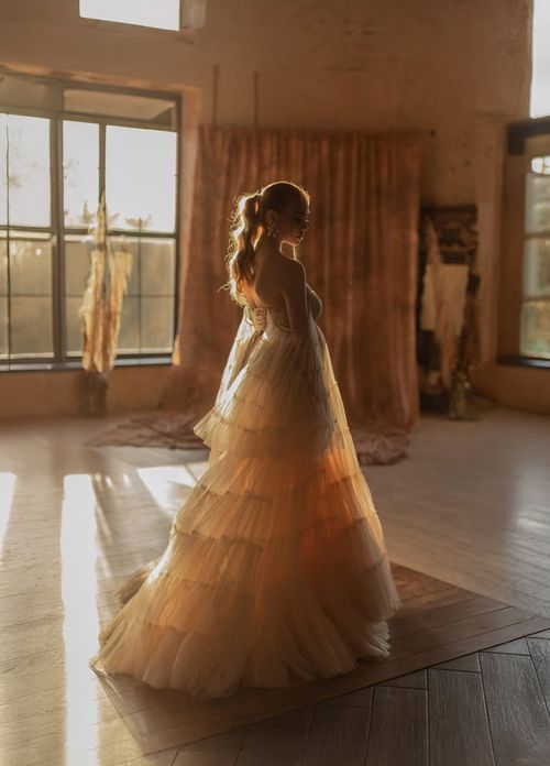 Beautiful wedding gowns in warm sunlight create silhouettes across empty dance studio floor.