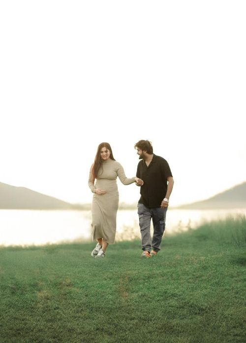 A couple sit and run together across a grassy hilltop silhouetted against a glowing sunset sky.
