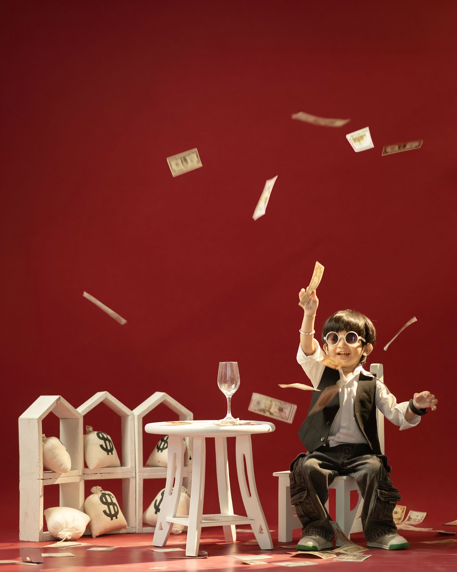 A toy figurine in a suit throws money in the air beside miniature houses and a wine glass on a red background.
