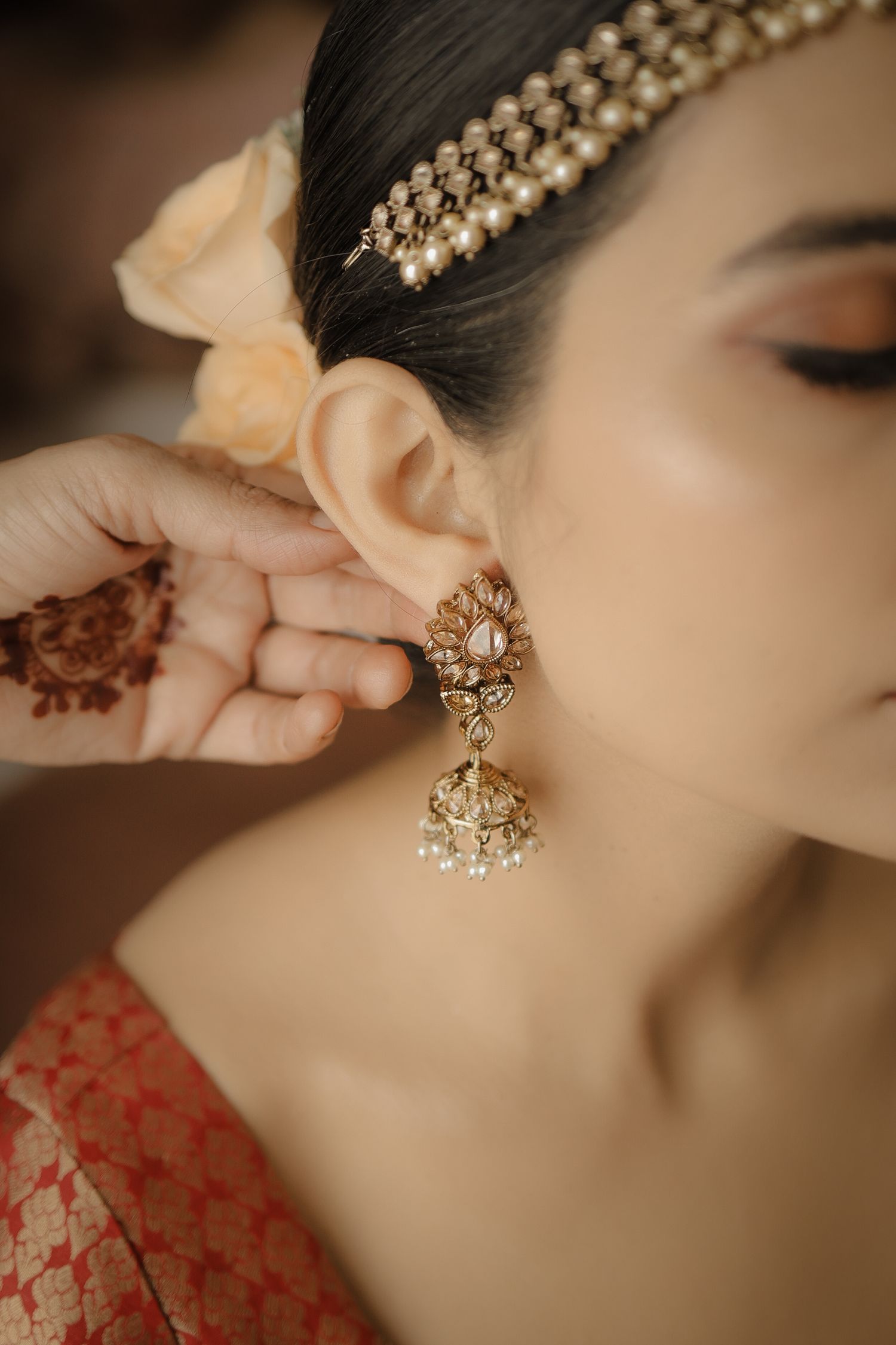 Close-up shots of ornate gold and pearl jhumka earrings being worn with a red traditional outfit.