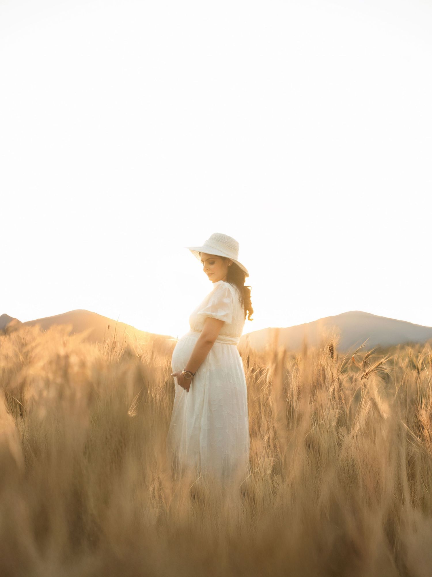 White dress photographed against a golden sunset in a field of tall grass for modern maternity photoshoot.