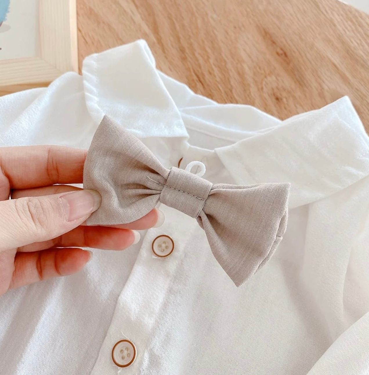 Step by step tutorial showing how to tie a white bow tie accessory on a light colored shirt.