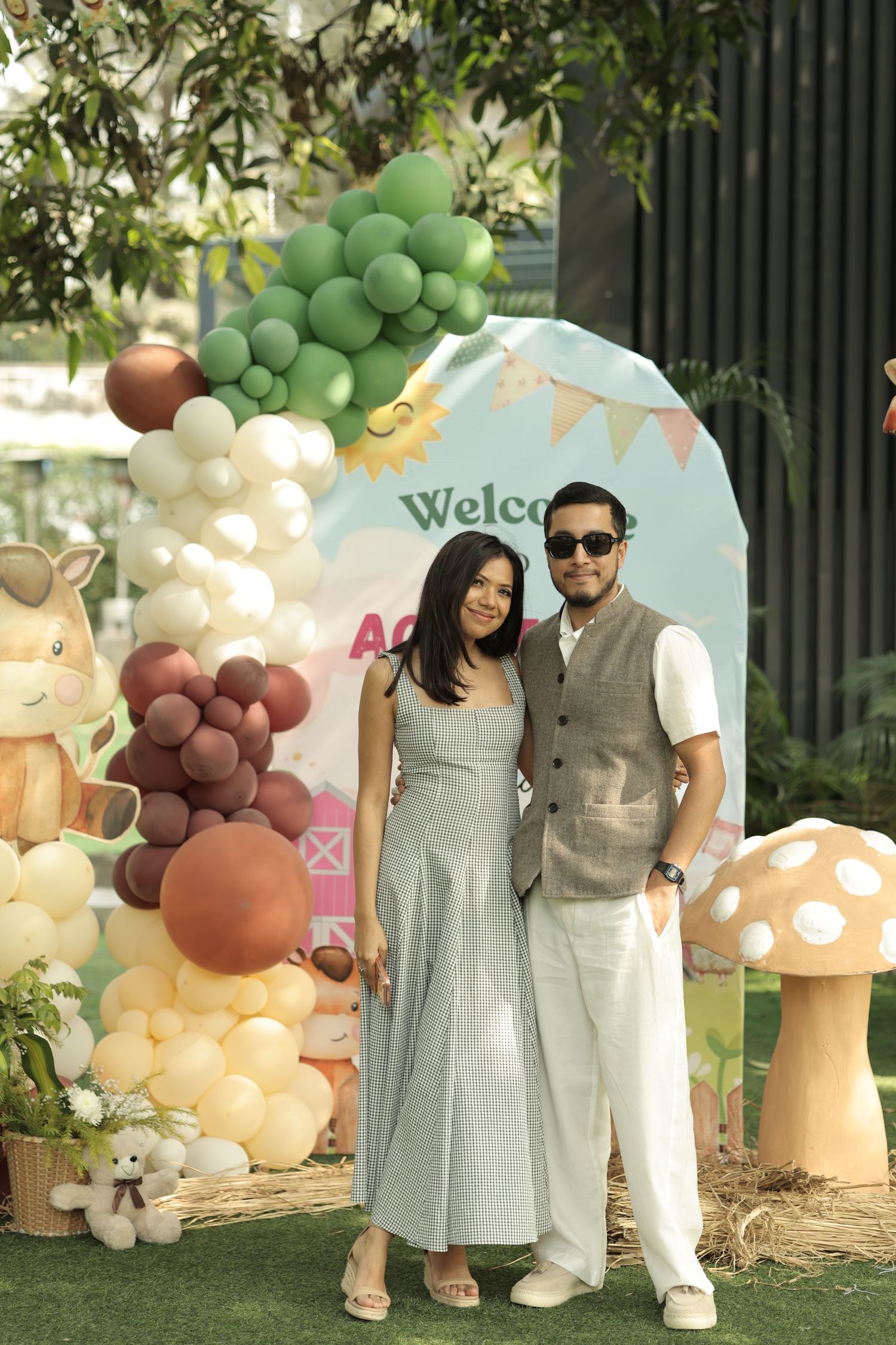 Couple posing together at a festive welcome party with colorful balloon arch and woodland themed decorations.