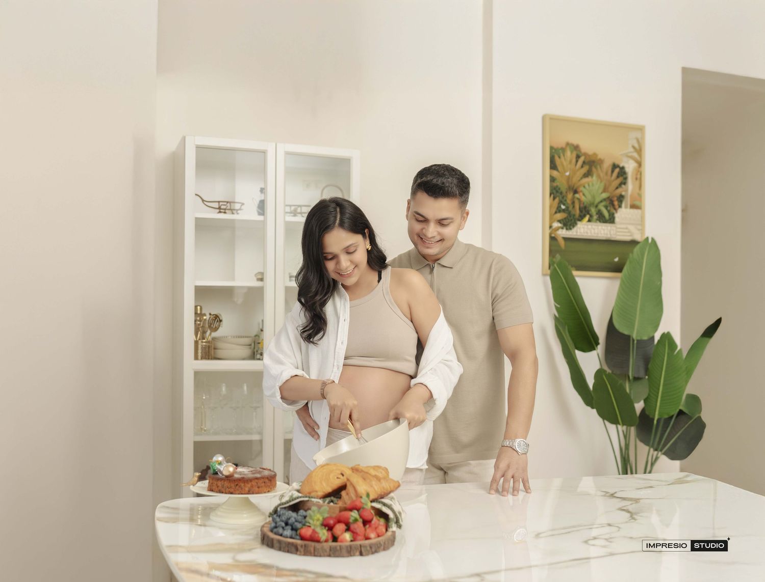 Pregnant couple standing at kitchen counter with fresh fruit and croissants in a bright modern home.