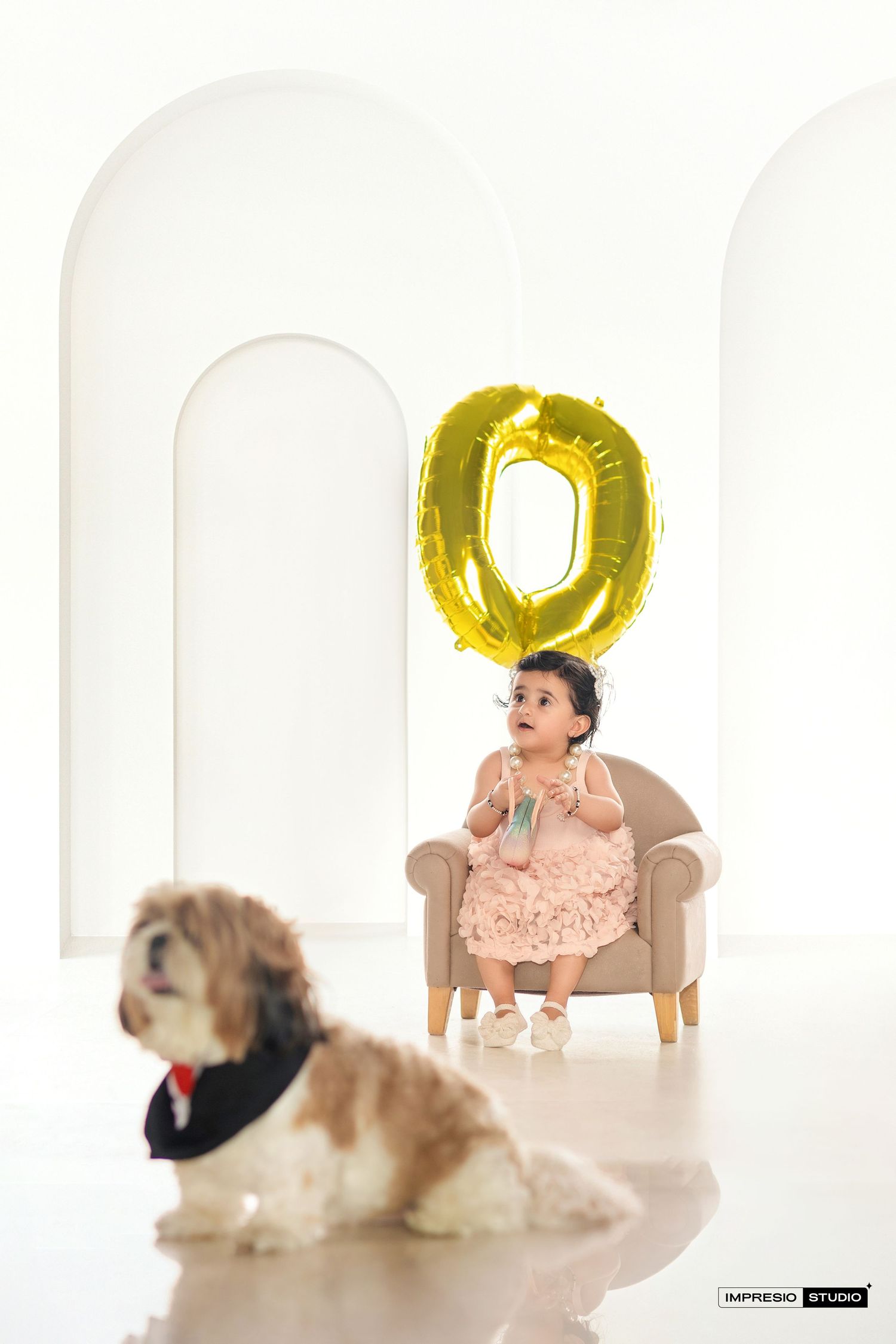 A baby and dog sit together in a bright white studio setting with gold balloon letters as decorative elements.