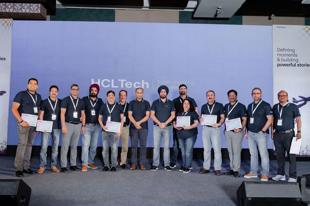 A group of professionals in business casual attire stand together on stage at a HCL Tech corporate event.
