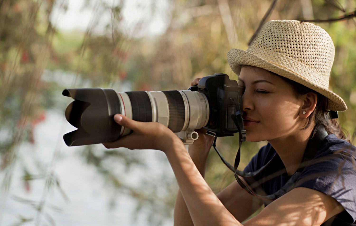 Wildlife photographer wearing a sun hat captures images of birds with a professional telephoto lens in nature.