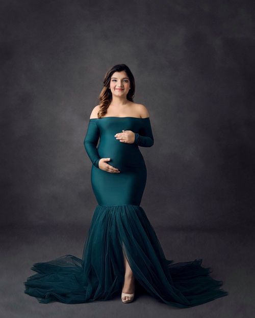Off-shoulder teal mermaid maternity gown with dramatic tulle train in studio setting.