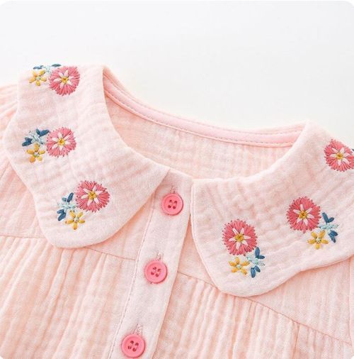 Close-up of pink baby romper collar with delicate floral embroidery and button details.