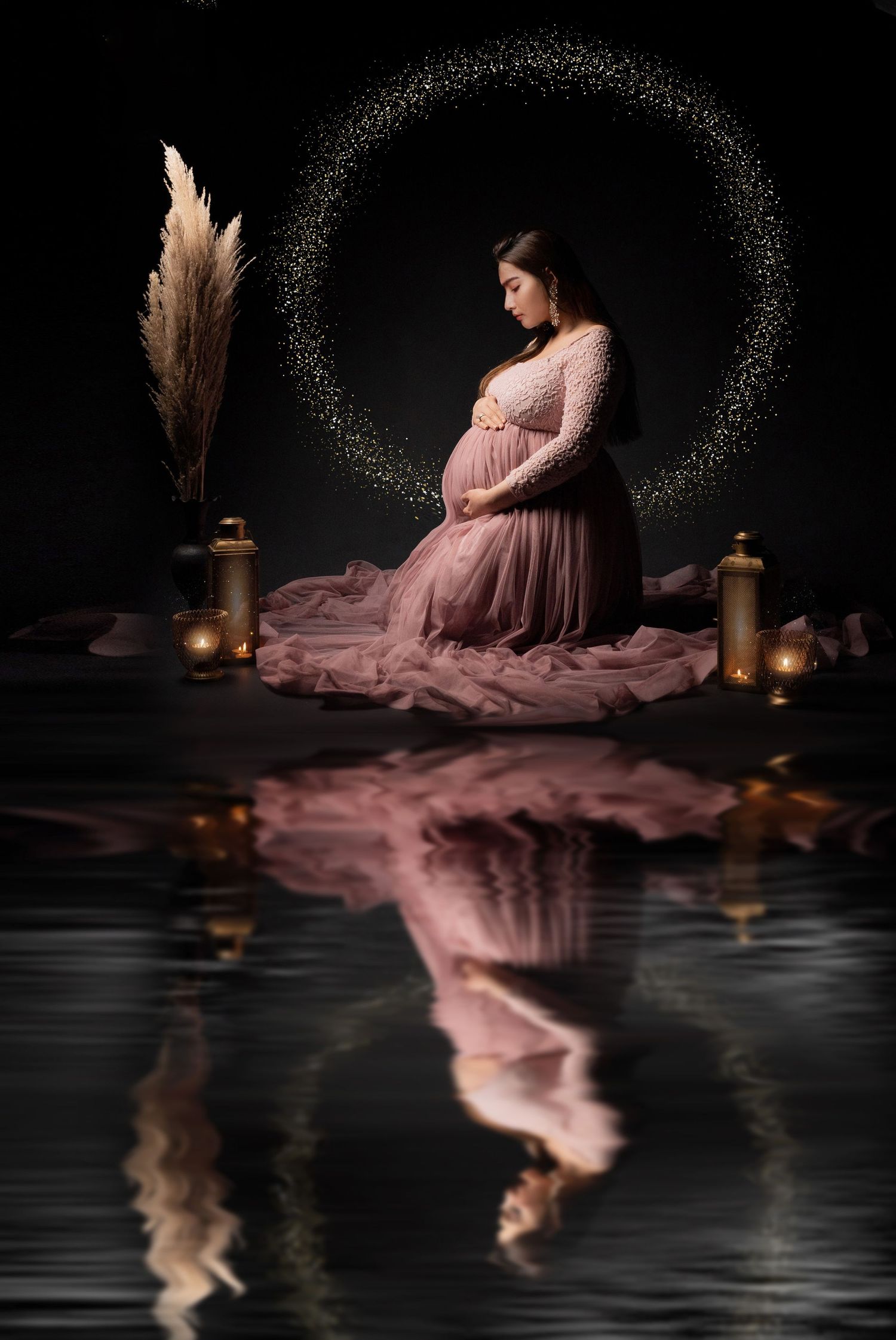 Artistic maternity photo with circular light halo, flowing pink dress and reflection on dark background.