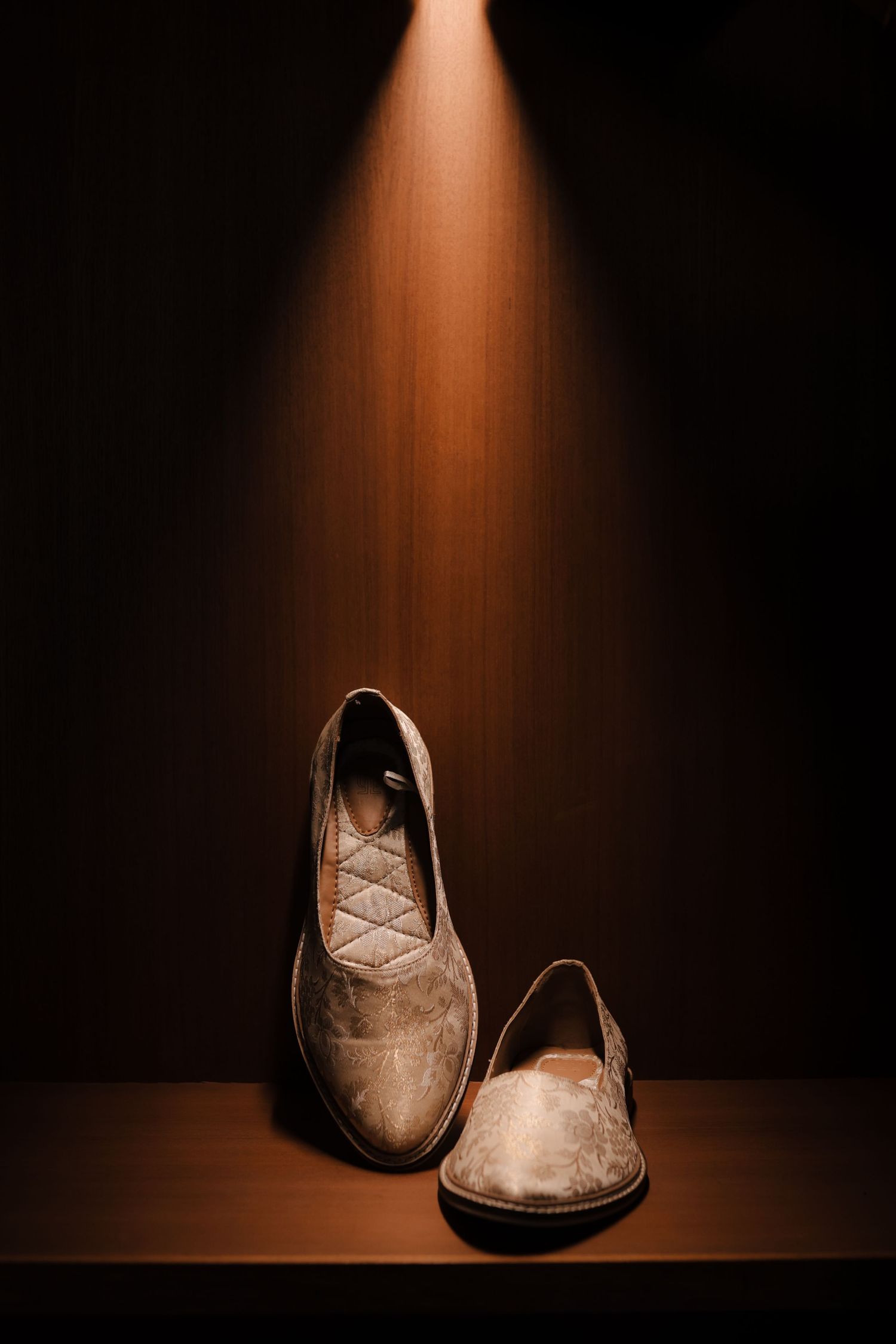 A pair of worn brown suede shoes dramatically lit by a single overhead spotlight against a dark background.