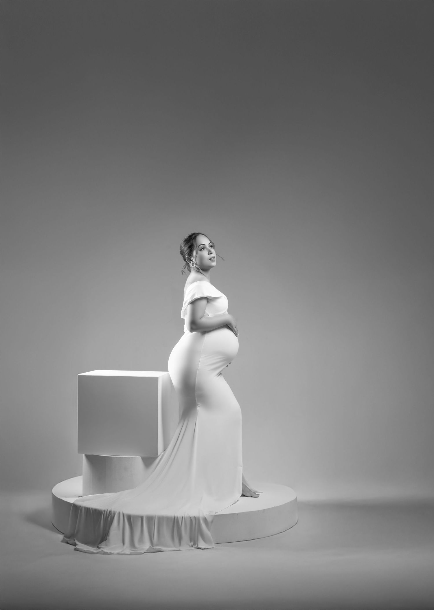 Artistic black and white maternity portrait on a minimalist curved platform setup.