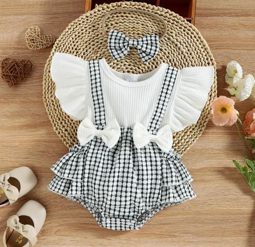 Vintage-style baby romper with gingham pattern and white ruffles displayed on woven mat.