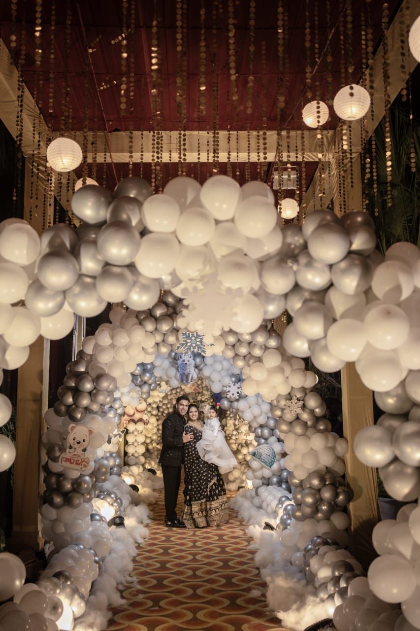 Couple poses under elegant white and silver balloon arch with hanging lanterns at a romantic wedding celebration.