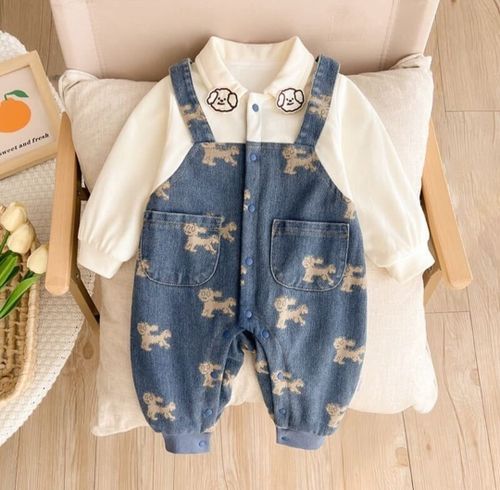 Adorable baby denim overalls with puppy print pattern paired with a white long sleeve shirt on a light cushioned surface.