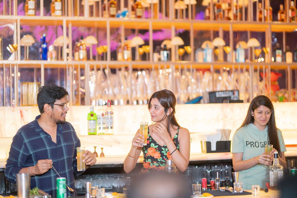 Three people socializing at a stylish bar with backlit shelves of bottles and warm ambient lighting.