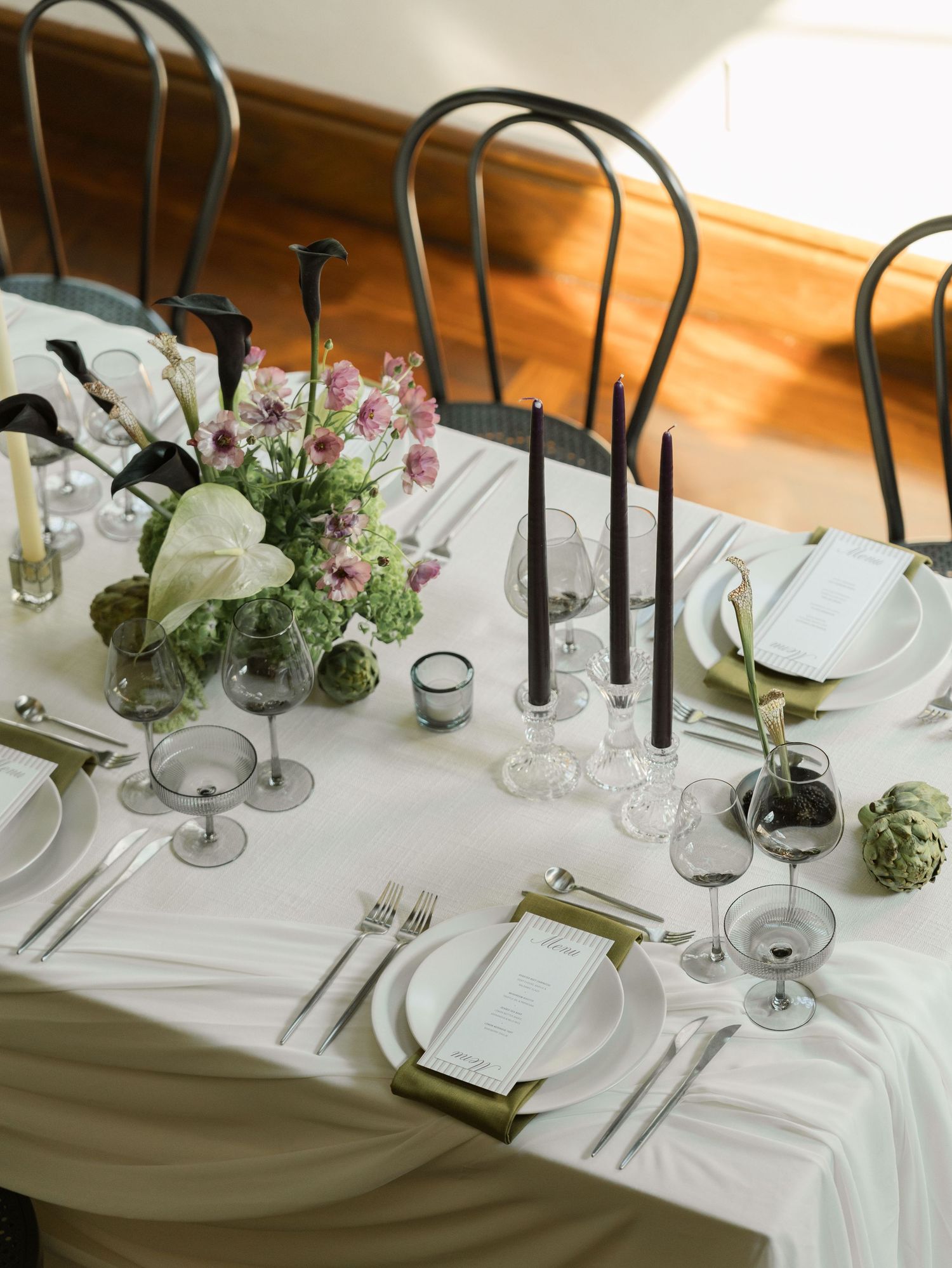 Elegant table setting with black chairs, white linens, and delicate floral centerpiece.