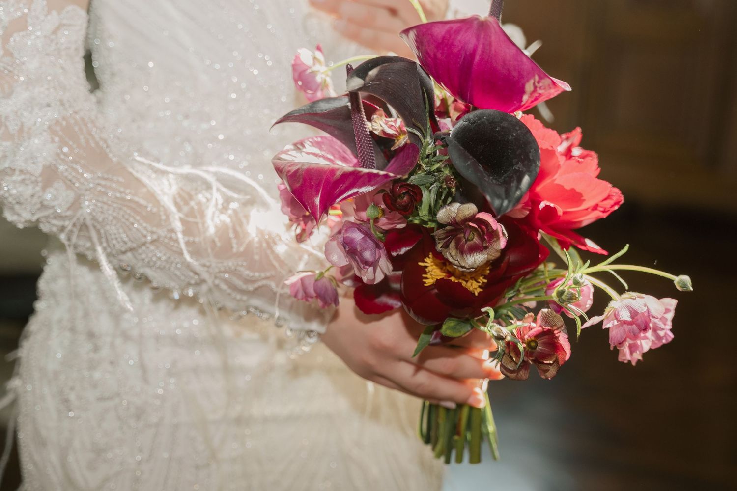 A bride in a white lace dress holds a vibrant bouquet of pink and burgundy flowers with cascading greenery.