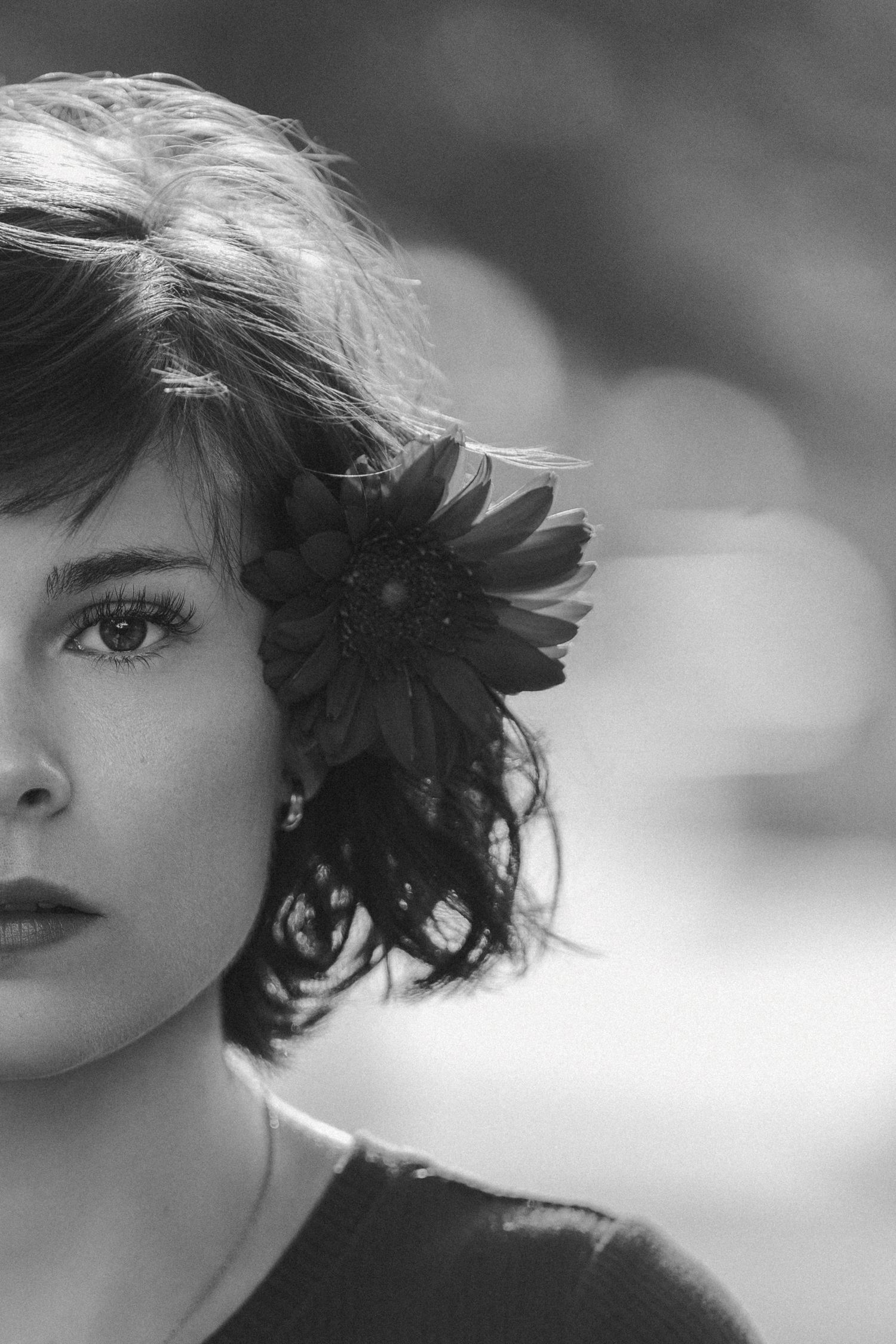 A black and white artistic portrait showing an eye and windswept hair against a soft blurred background.