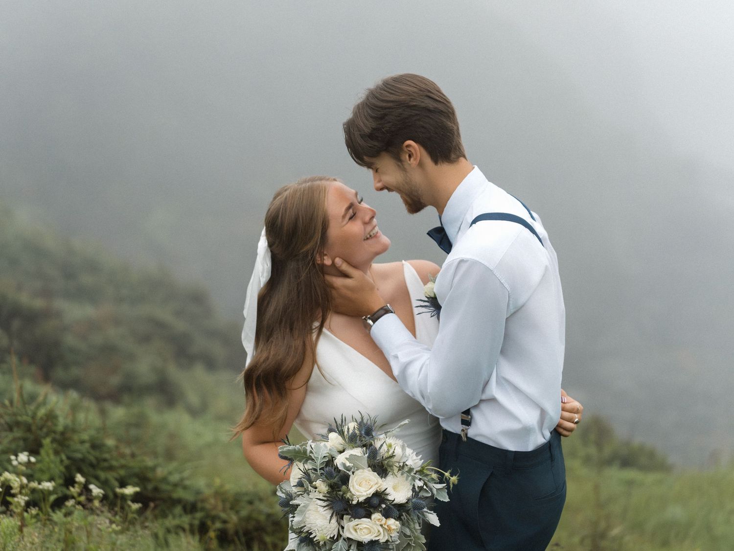 A romantic couple kisses on a misty mountainside during an intimate engagement or wedding photo session.