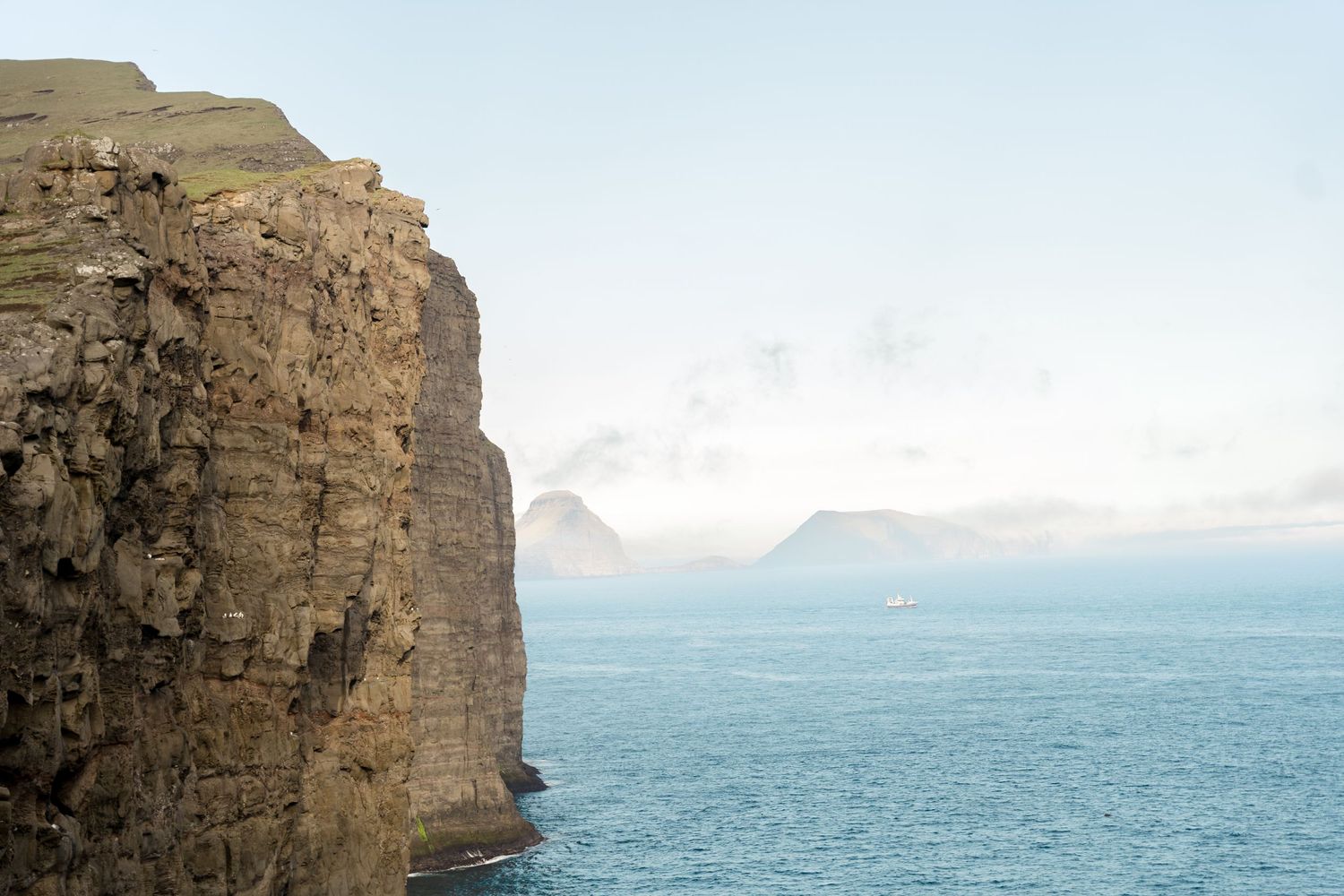 Dramatic rocky cliffs overlooking a misty blue ocean with distant islands in the background.