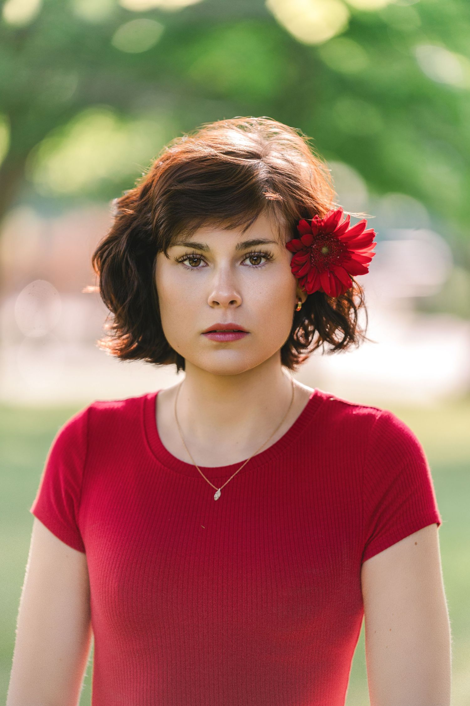 Portrait in a red top with a vibrant red gerbera daisy flower in dark hair against a soft bokeh background.