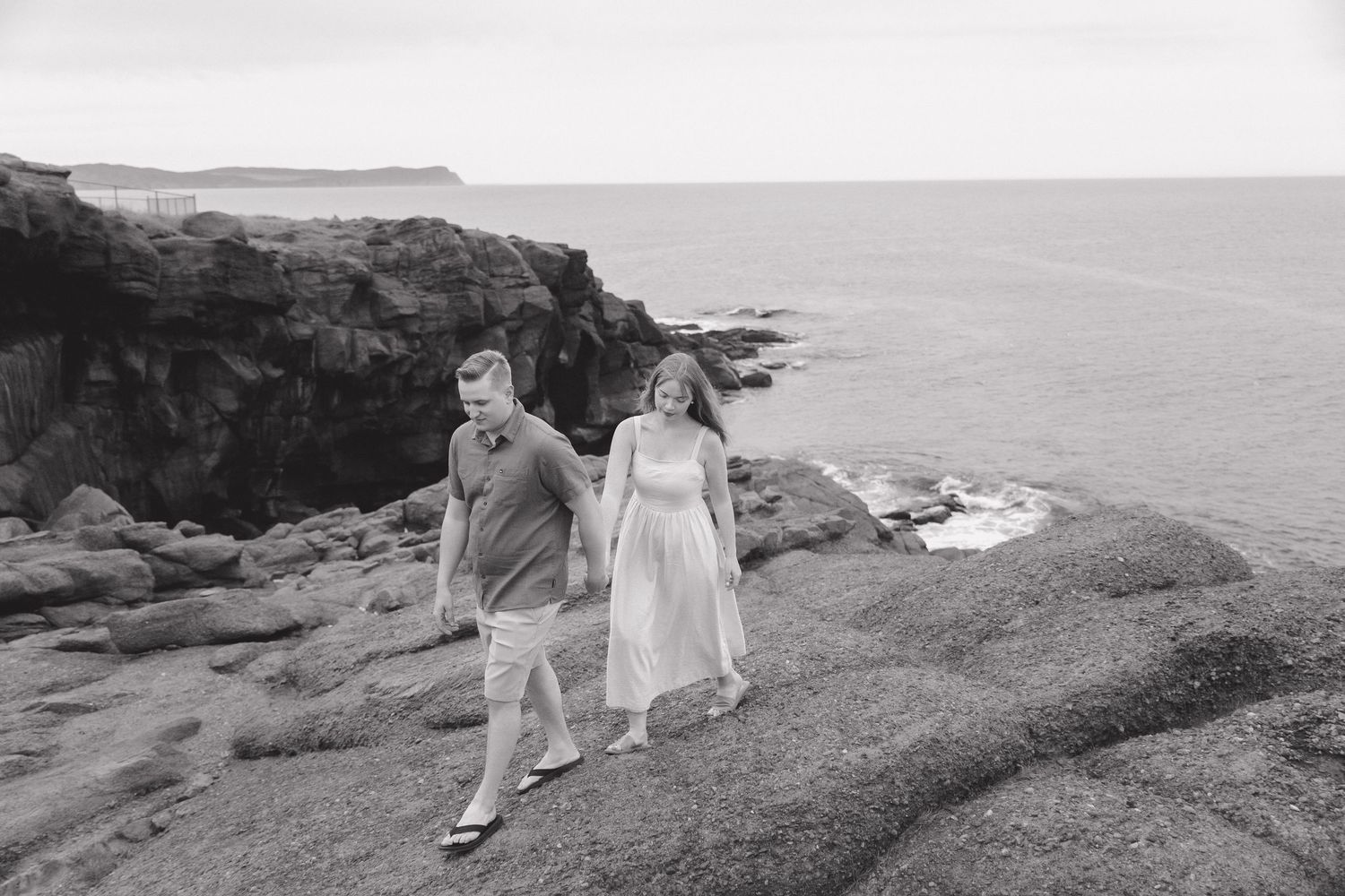 A couple walks along rugged coastal cliffs with dramatic ocean views in the background.