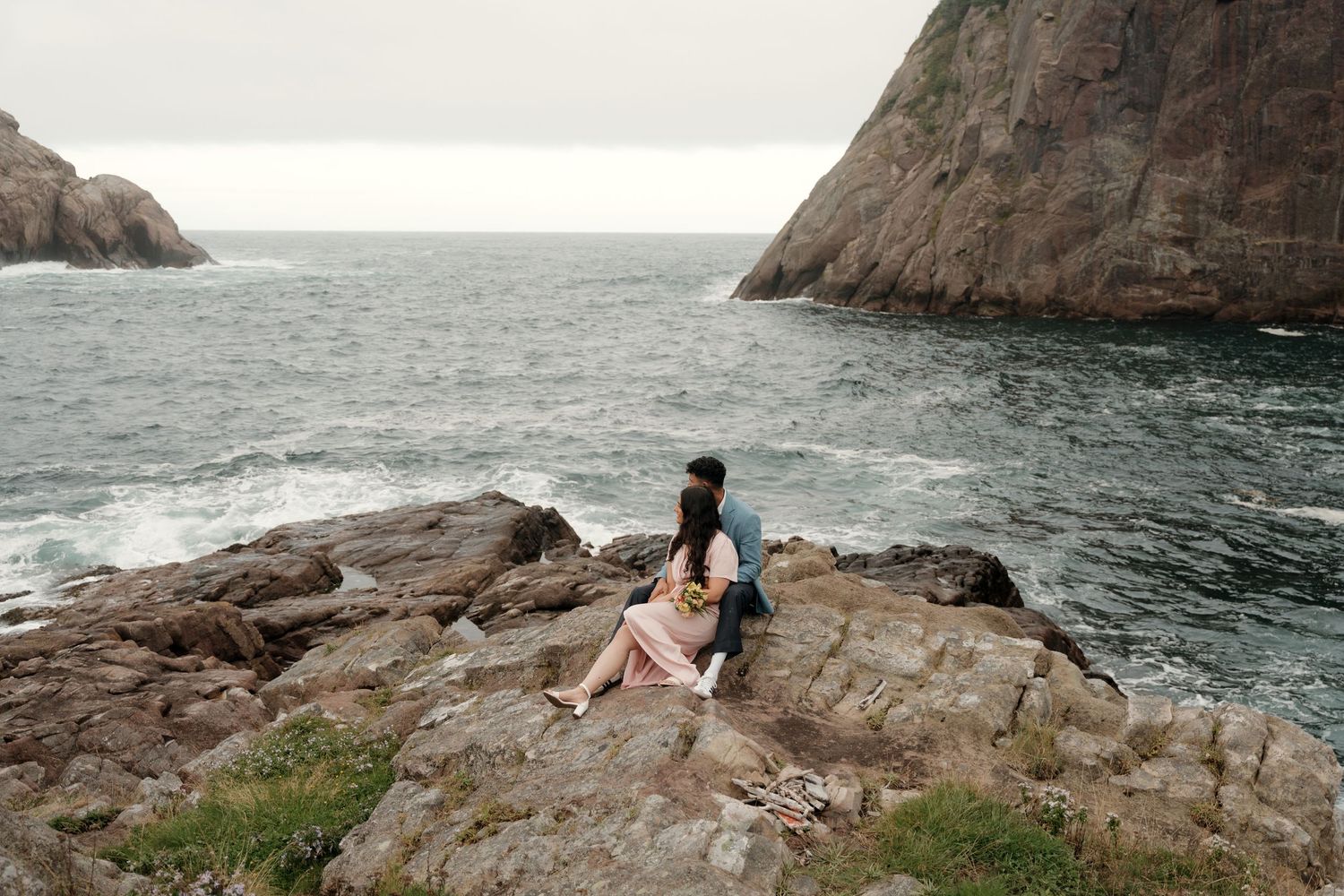 Dramatic coastal photoshoot of a person posing on rocky cliffs overlooking the ocean at sunset.