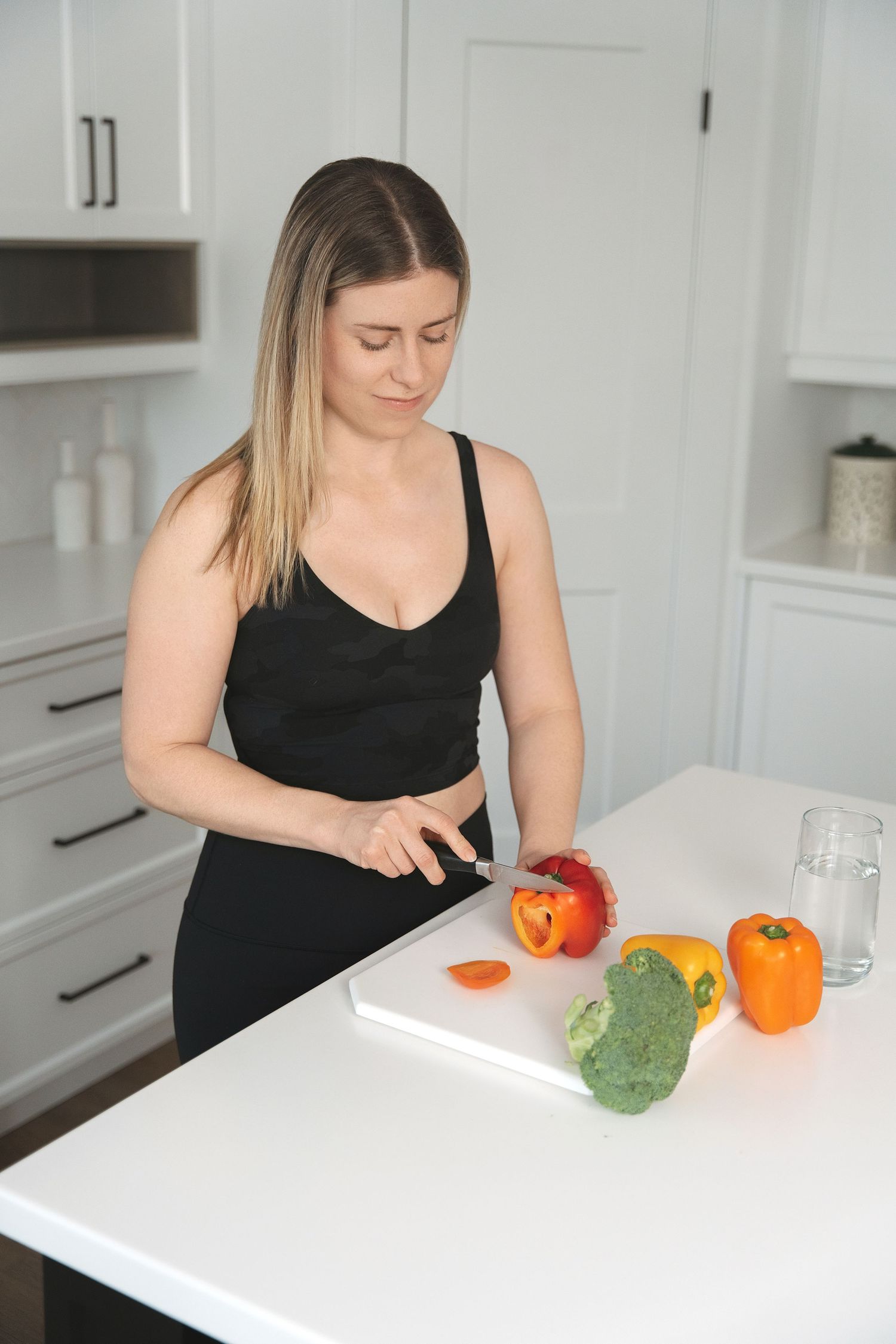 Person in black tank top chopping fresh vegetables on white kitchen counter.