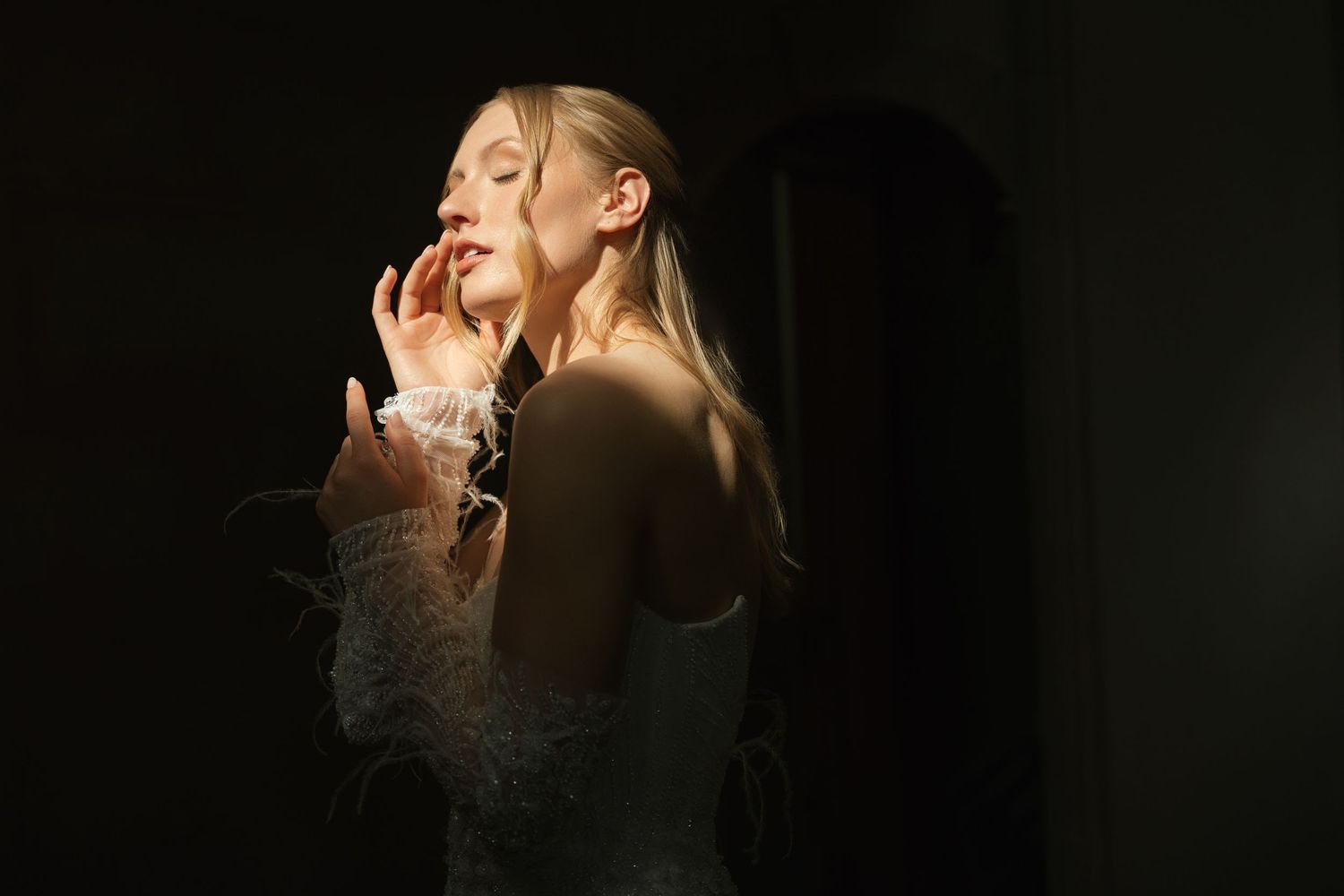 A couple shares a romantic kiss in front of a dark background in a dramatic artistic portrait.