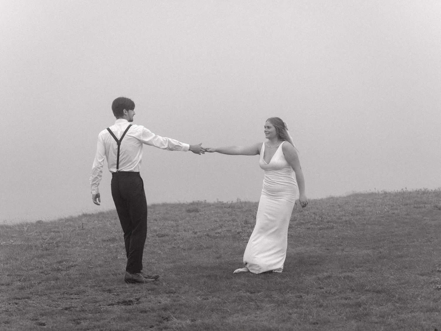 A couple creates whimsical poses on a hilltop in dramatic black and white photography.