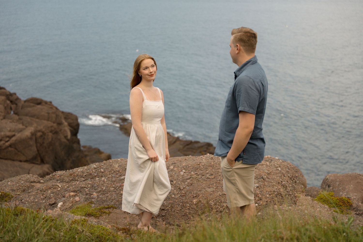 Two people stand together on a scenic cliffside overlooking the ocean during a cloudy day.
