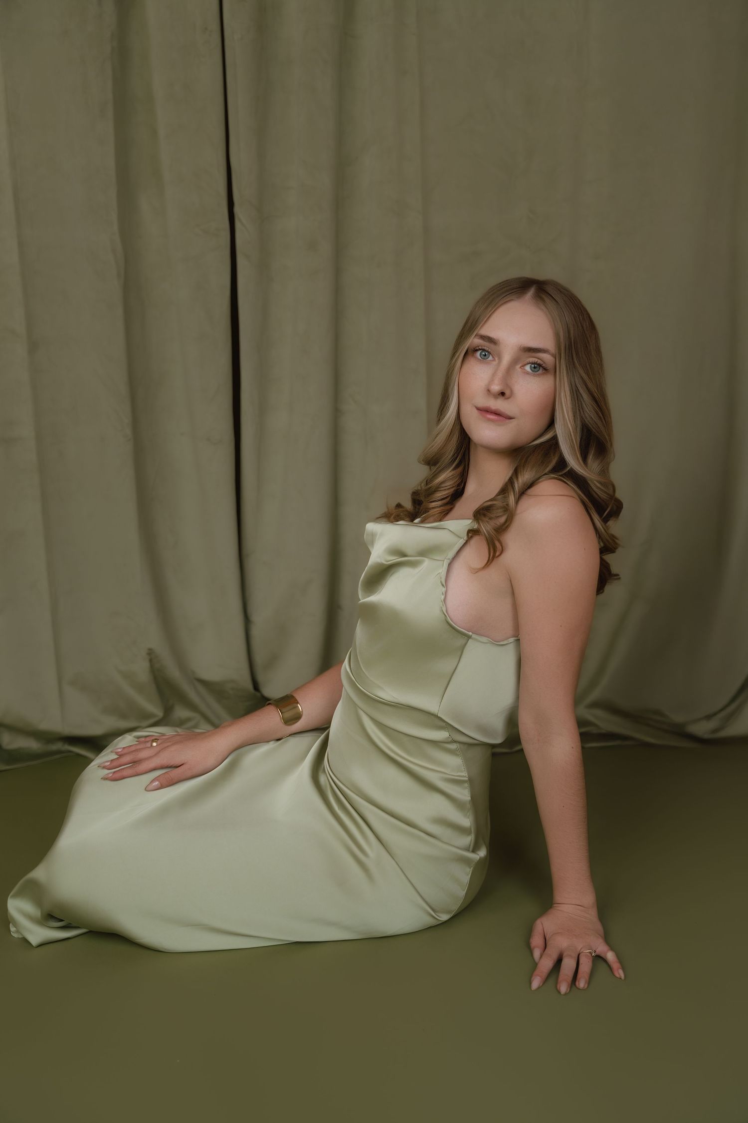 Studio portrait series showing a person in a light sage green dress posing gracefully against a draped fabric backdrop.