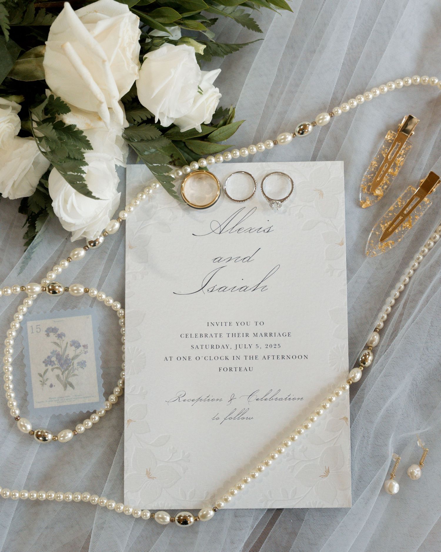 Elegant wedding invitation with pearl necklaces, white roses, and gold accessories on soft tulle fabric.