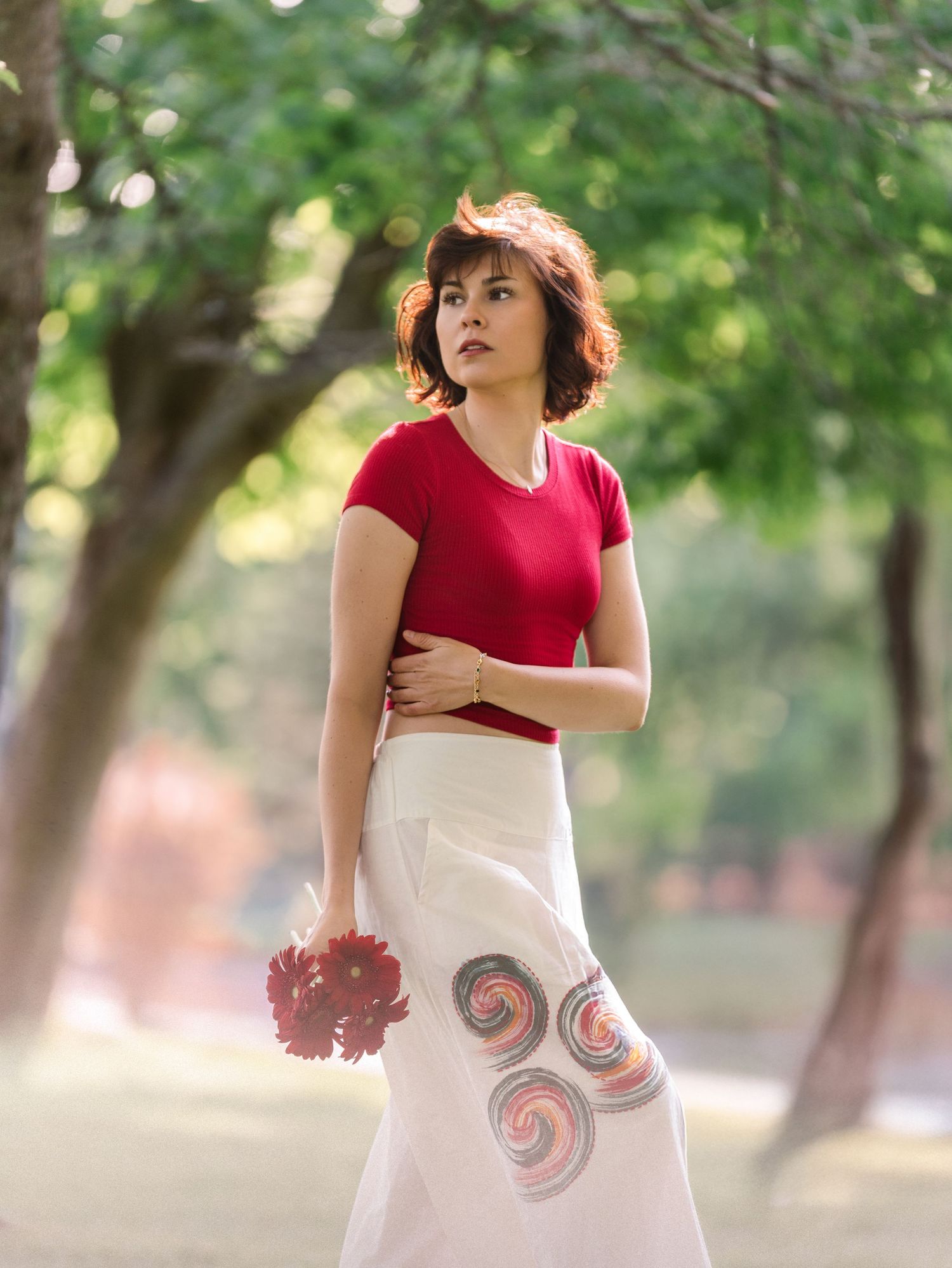 A person in a red top and white skirt dances gracefully outdoors with trees in the background.