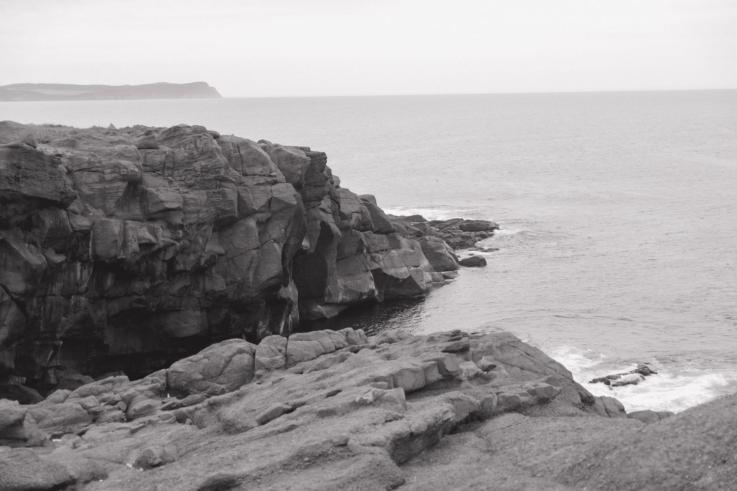 A dramatic panorama of rugged coastal cliffs and rocky shores stretches along the misty ocean horizon.