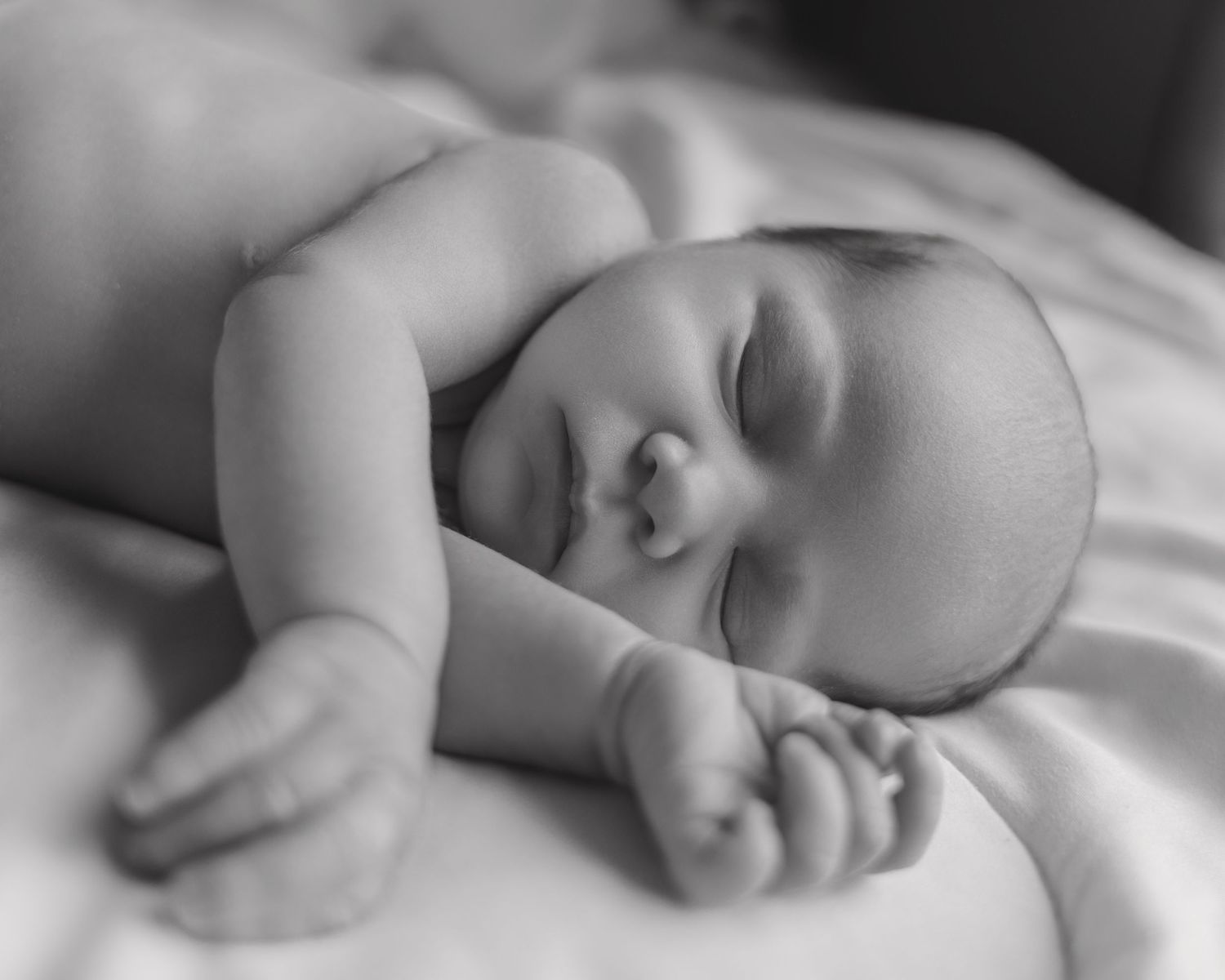 Black and white photo of a peaceful sleeping newborn baby lying on a soft white blanket.