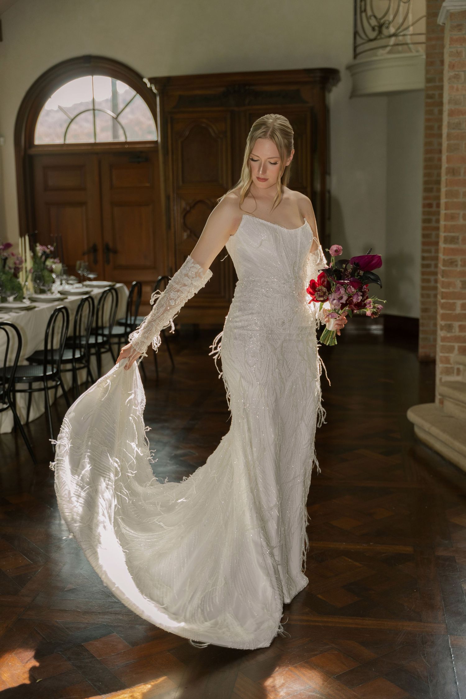 A bride in a flowing white lace wedding dress twirls gracefully across a rustic wooden floor in an elegant venue.