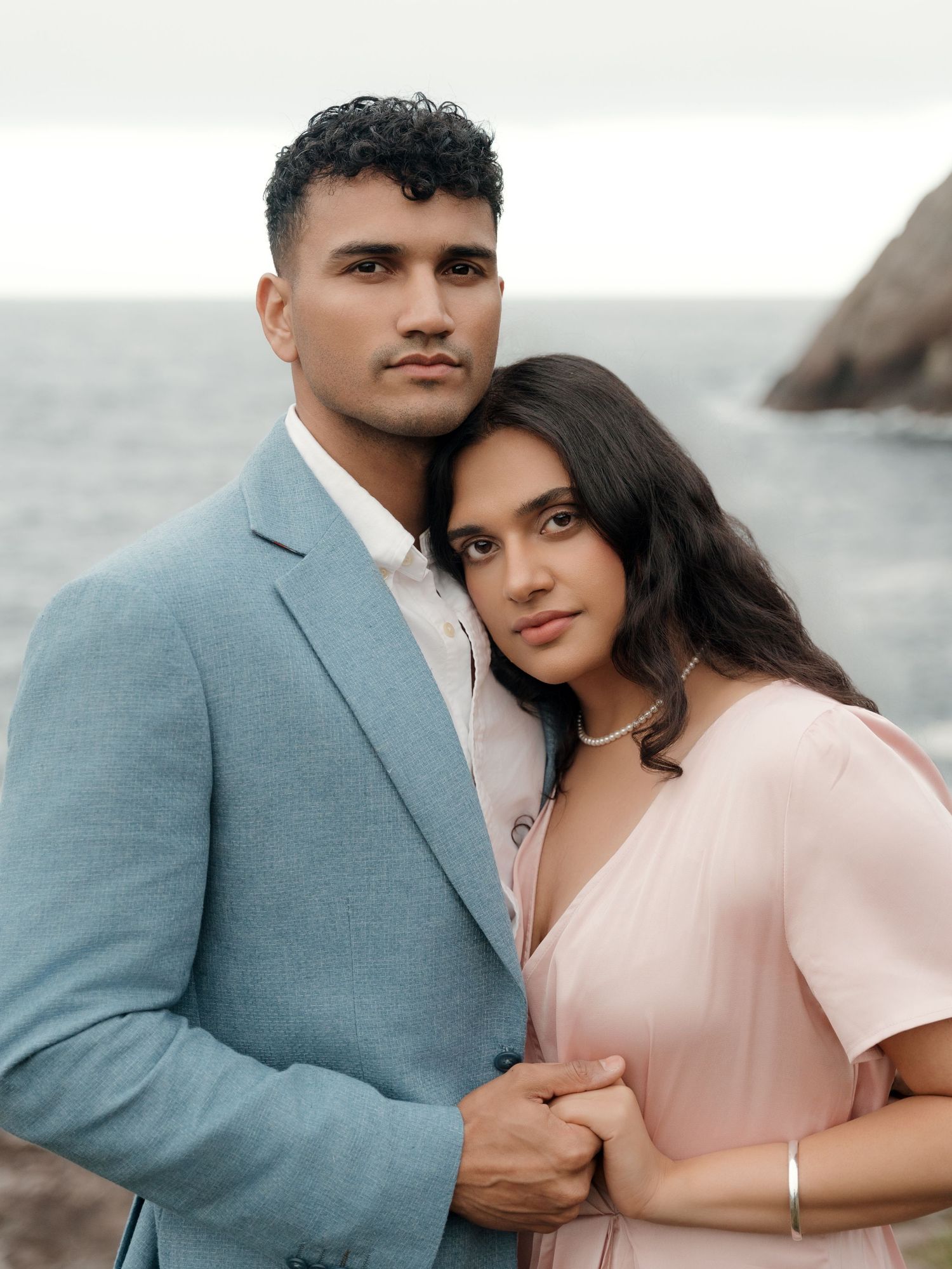 A romantic couple in coordinated pink and gray outfits embrace on the beach during a photo session.