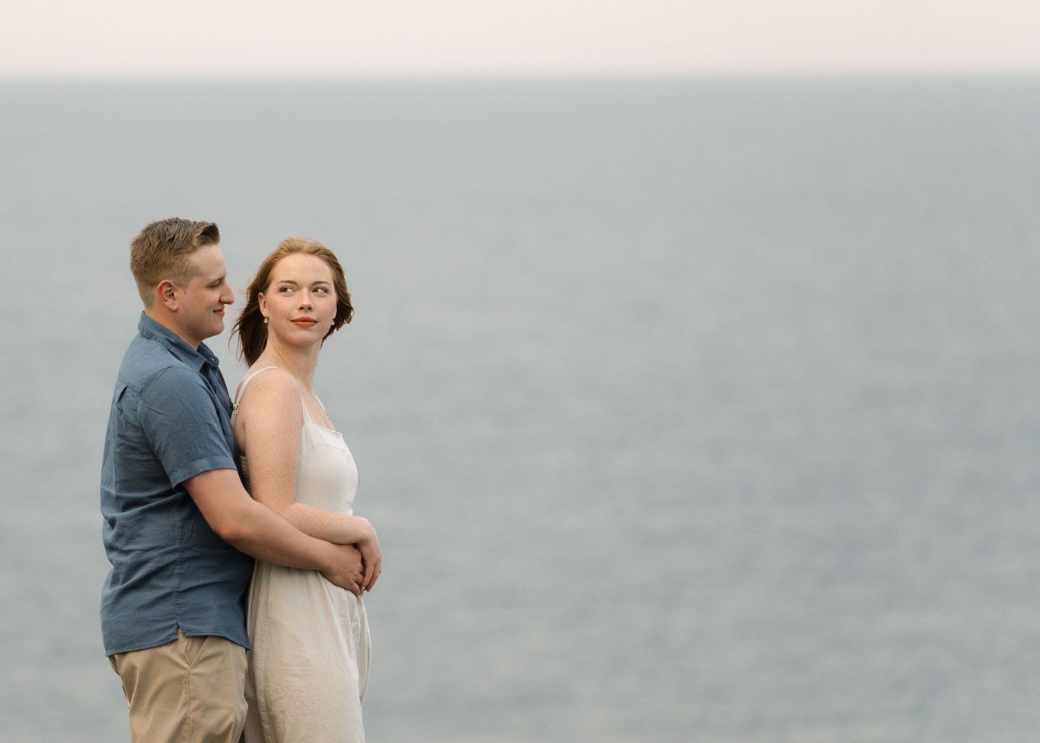 A loving couple dressed in casual attire embrace during their coastal engagement photo session.