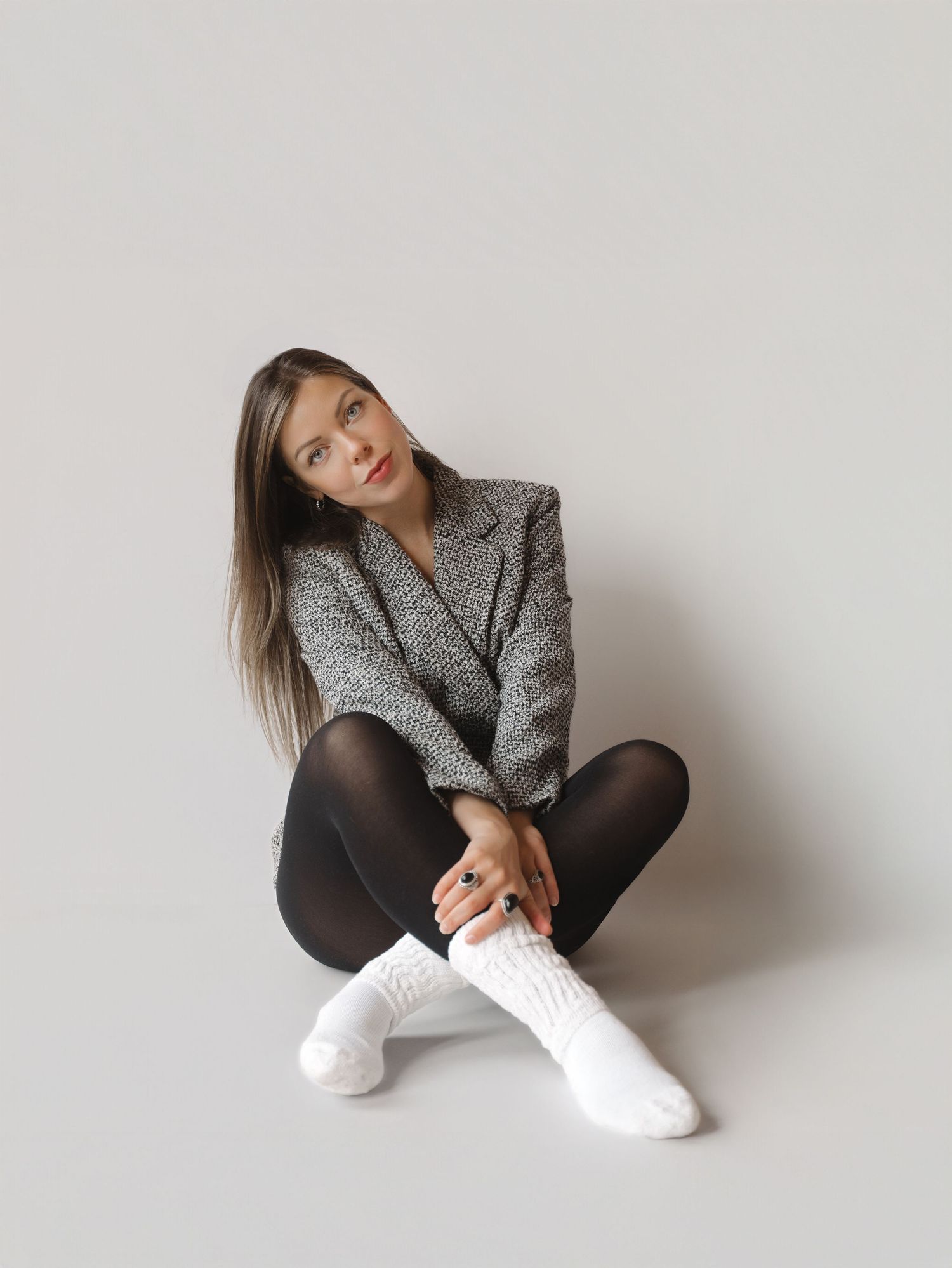 A model in a gray tweed blazer and black tights poses against a white wall in a series of artistic shots.