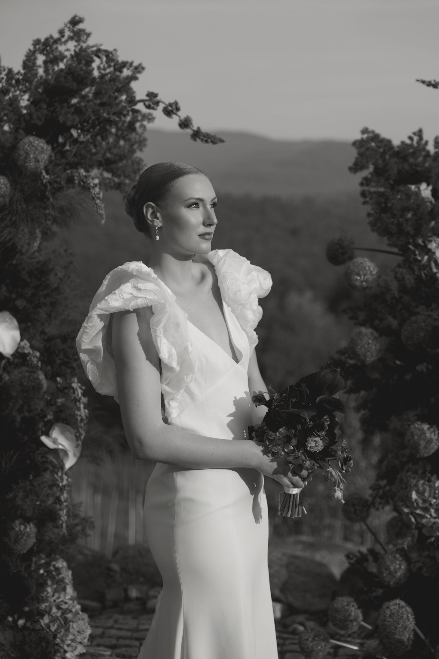 A captivating black and white portrait series of a person in a white ruffled dress against a dreamy outdoor backdrop.