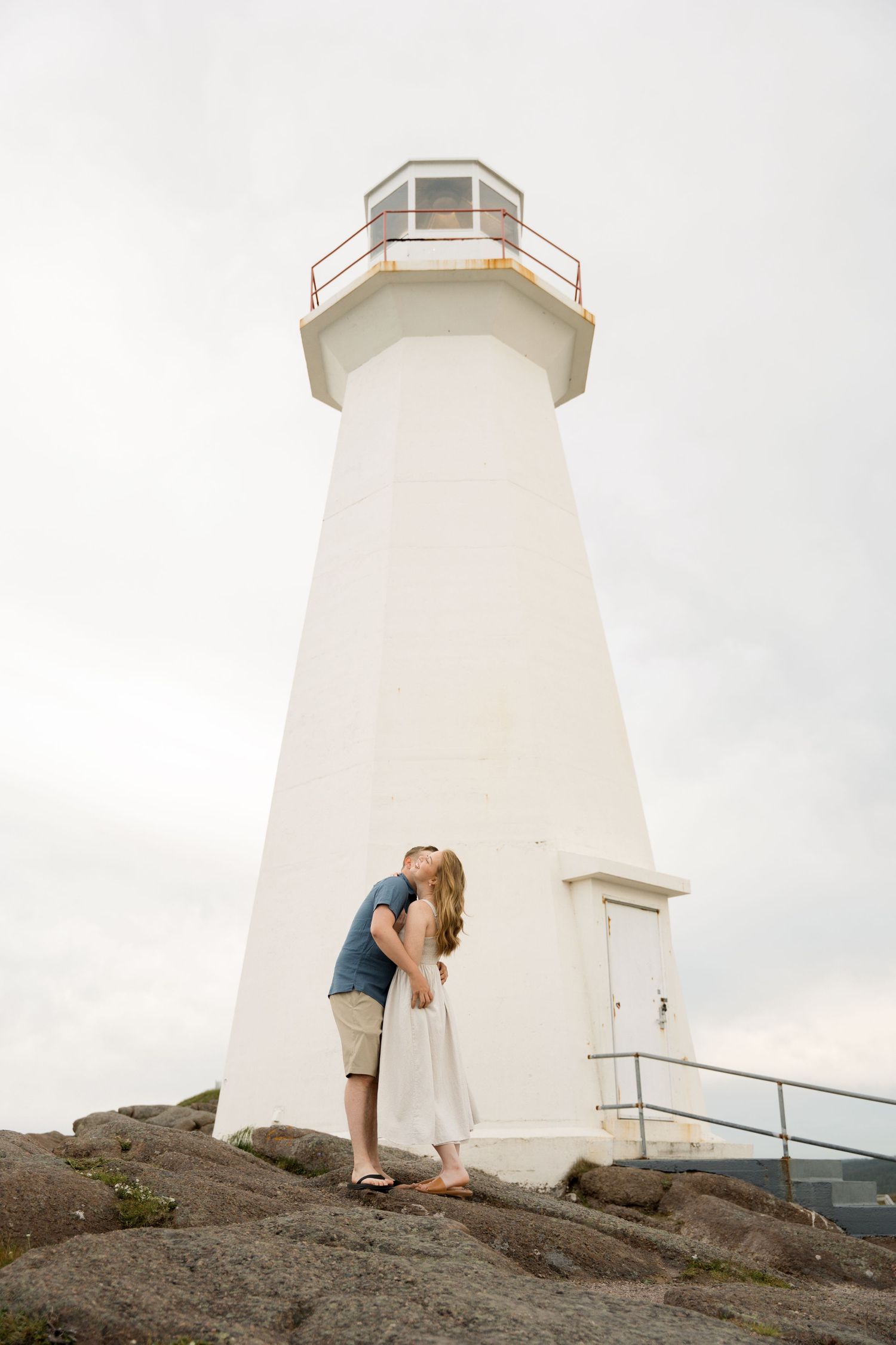 Four progressive shots show a person exploring a coastal lighthouse from different angles against an overcast sky.