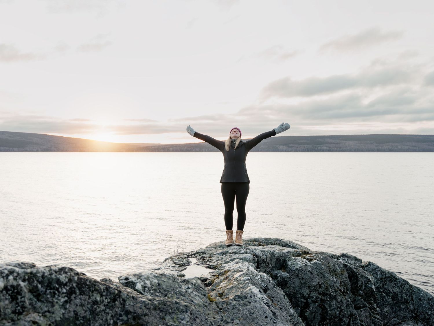 Silhouette of person celebrating with arms raised against dramatic coastal sunset.
