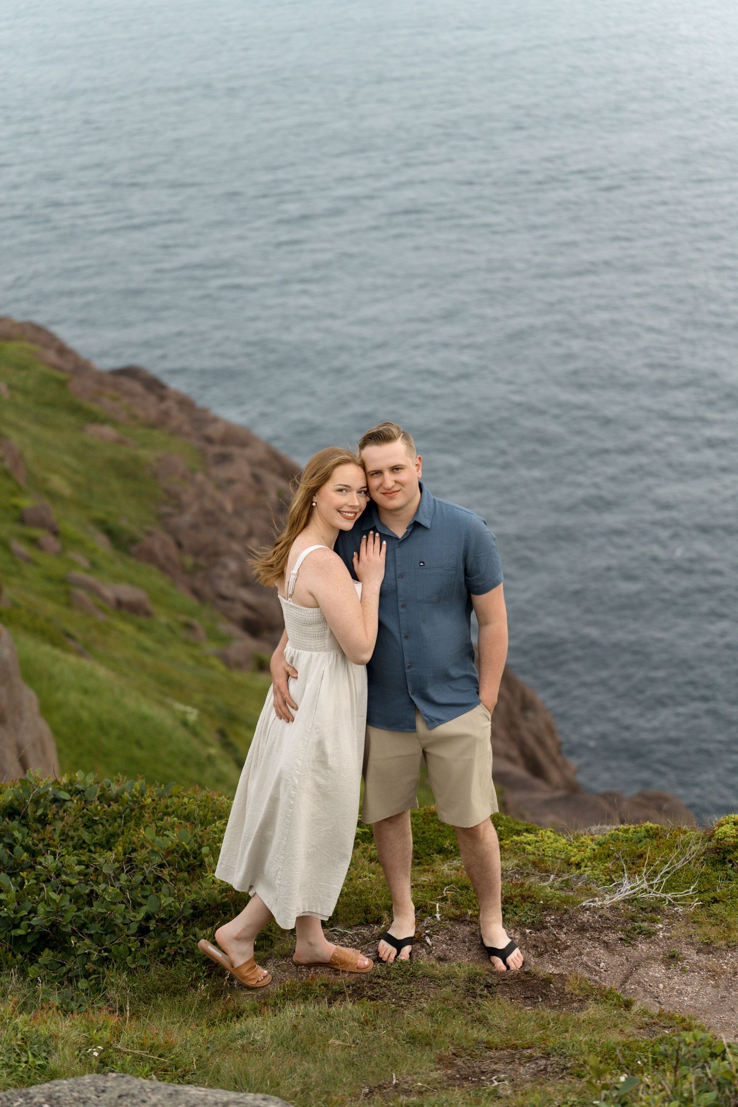 A couple shares a romantic moment on the edge of a scenic coastal cliff overlooking the ocean.